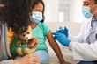 © Wavebreak Media - Hispanic male doctor giving covid vaccination to daughter patient with mother, wearing face masks