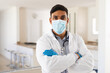 © Wavebreak Media - Portrait of hispanic male doctor wearing face mask standing with arms crossed looking to camera