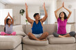 © Wavebreak Media - Smiling hispanic daughter and parents practicing yoga sitting on couch in living room