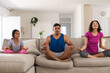 © Wavebreak Media - Happy hispanic daughter and parents practicing yoga sitting on couch in living room