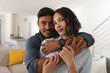 © Wavebreak Media - Portrait of happy hispanic couple embracing in living room, looking to camera