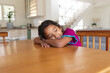 © Wavebreak Media - Smiling hispanic girl sitting at table in kitchen resting head on ams, looking away