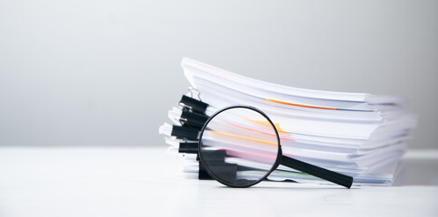 Stack of report paper documents with magnifying glass.