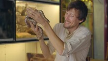 A Man Visits A Cafe With Exotic Animals. Cafe Where You Can Contact With Animals. He Is Touching A Snake.