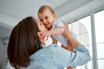 Loving mom carying of her newborn baby at home.Mom and baby boy playing in sunny bedroom. Parent and little kid relaxing at home. Family having fun together. Childcare, maternity concept.