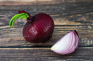 Red onions on the wooden board.  Whole and sliced onions with green young leaves and water drops. Flat lay, copy space
Mars onions.