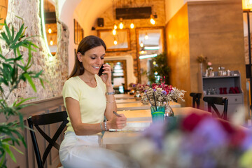 Wall Mural - Happy woman in cafe talking on phone. Attractive woman sitting in a cafe with a cell phone.