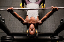 Determined Young Man Doing Bench Press While Listening Music Through Headphones In Gym