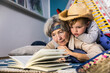 © Stefanie Aumiller/Westend61 - Senior woman reading book while boy lying on her at home