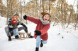 © Frank van Delft/Westend61 - Playful boy on snow while father sitting with younger son on sled in background