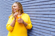 © Ignacio Ferrandiz Roig/Westend61 - Smiling woman holding juice in disposable cup leaning on brick wall while looking away