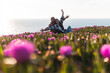 © Josu Acosta/Westend61 - Young couple with arms outstretched sitting at flower filed by sea