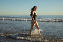 Mid Adult Model In One Piece Swimsuit Walking In Water During Sunset