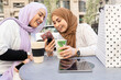 © Jose Carlos Ichiro/Westend61 - Arab women with coffee cup using smart phone at sidewalk cafe in city