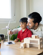 © Jose Carlos Ichiro/Westend61 - Smiling male architect discussing over wind turbine model with son at home