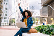 © COROIMAGE/Westend61 - Young woman cheering while using laptop in city