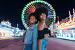 © Julio Rodriguez/Westend61 - Smiling female friends standing back to back in amusement park at night