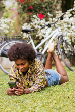 Woman Using Mobile Phone While Lying On Grass In Garden