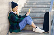 © Javier Sanchez Mingorance/Westend61 - Smiling woman in knit hat using mobile phone on steps