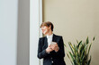 © Eugenio Marongiu/Westend61 - Happy female business professional looking away while holding mobile phone against beige wall in office