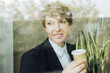 © Eugenio Marongiu/Westend61 - Smiling female business professional looking away while holding disposable coffee cup seen through glass window