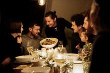 Smiling Men And Women Looking At Pasta Held By Mature Man In Kitchen