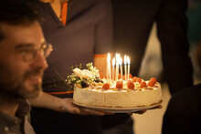 Birthday Cake Held By Mature Woman By Male Friend In Birthday Party At Home
