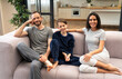 © OneInchPunch/Westend61 - Happy family sitting on sofa in living room at home