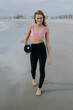 © OneInchPunch/Westend61 - Woman holding exercise mat while walking on shore at beach