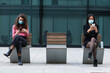 © NOVELLIMAGE/Westend61 - Young women wearing protective face mask using mobile phone while sitting with social distancing on bench