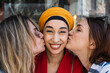 © NOVELLIMAGE/Westend61 - Female friends kissing beautiful woman on cheek outdoors