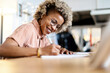 © Rafael Fernandez Torres/Westend61 - Businesswoman with eyeglasses writing while working at home office