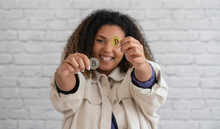 Smiling Woman Showing Silver And Gold Colored Bitcoins In Front Of Wall