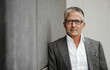 © Sandro Jodicke/Westend61 - Businessman wearing eyeglasses leaning on gray wall
