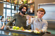 © Francesco Buttitta/Westend61 - Male bartender looking at trainee putting apples in glass jar at bar counter