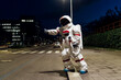 © Eugenio Marongiu/Westend61 - Female astronaut in space suit hailing ride while standing on footpath near road at night