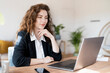 © steve brookland/Westend61 - Businesswoman with hand on chin looking at laptop in home office