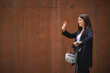© SERGIO NIEVAS/Westend61 - Young businesswoman waving hand while standing with electric push scooter by wall