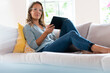 © steve brookland/Westend61 - Beautiful woman with digital tablet relaxing on sofa in living room