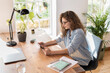 © steve brookland/Westend61 - Young businesswoman with eyeglasses looking at digital tablet in home office