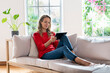 © steve brookland/Westend61 - Blond woman with digital tablet sitting on sofa in living room