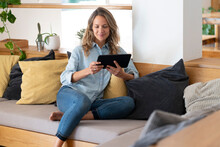 Relaxed Woman Watching Video Through Tablet While Sitting On Couch In Living Room