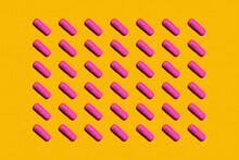 Pattern Of Rows Of Pink Medicine Capsules Laid Against Yellow Background