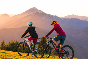 Wall Mural - Mother and daughter cycling downhill with mtb bikes at a sunset.