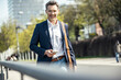 © Uwe Umstatter/Westend61 - Smiling businessman holding mobile phone while standing on sunny day