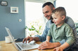 © Uwe Umstatter/Westend61 - Smiling male freelancer using laptop while sitting with son at home