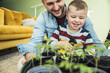 © Uwe Umstatter/Westend61 - Happy boy spraying water on potted plants while sitting with father in living room at home