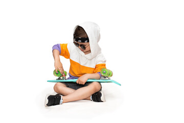 Wall Mural - Cute five year old kid boy in hip hop street style clothes sits with a turquoise skate on a white background.