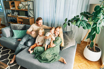 happy young family of four relaxing on a couch, couple playing with baby girl and toddler boy, top v