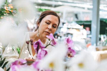 Wall Mural - Brunette middle aged woman in white dress buys lilac orchids potted house plants at the garden store